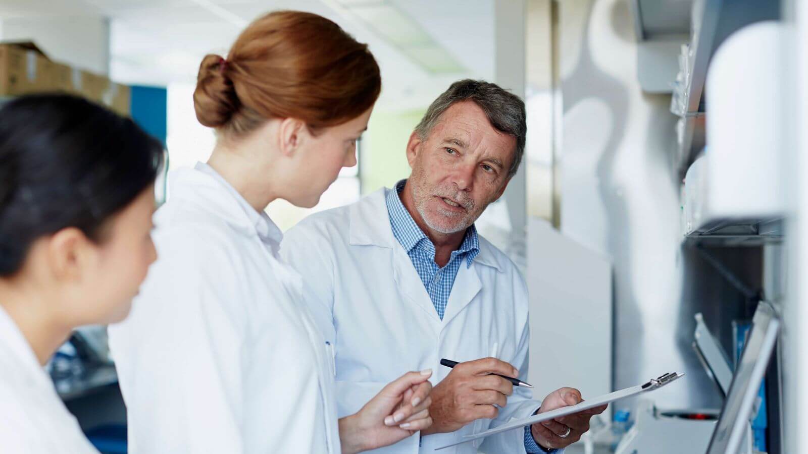 Pharmaceutical professionals in lab coats reviewing notes on clipboard