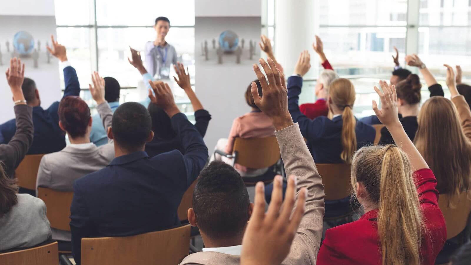 Audience raising hands during pharmaceutical conference presentation