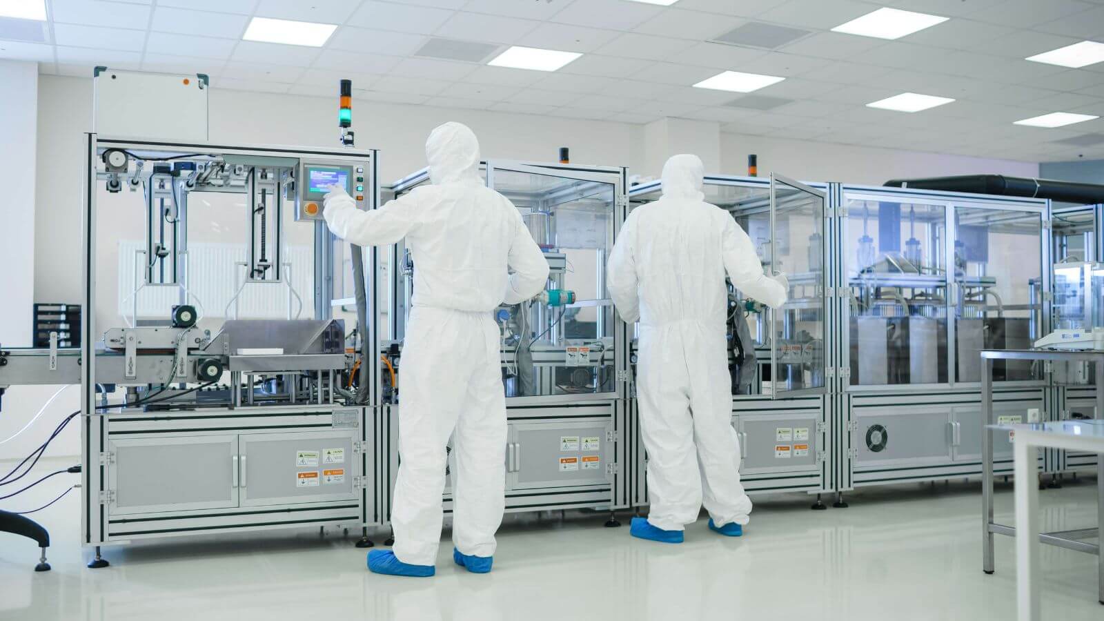 Two pharmacists in protective suits operating pharmaceutical production equipment
